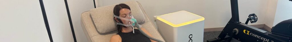 Person entspannt auf Liege mit Atemmaske für Zell- und Beckenbodentraining; neben Fitnessgerät und Cellgym-Kasten.